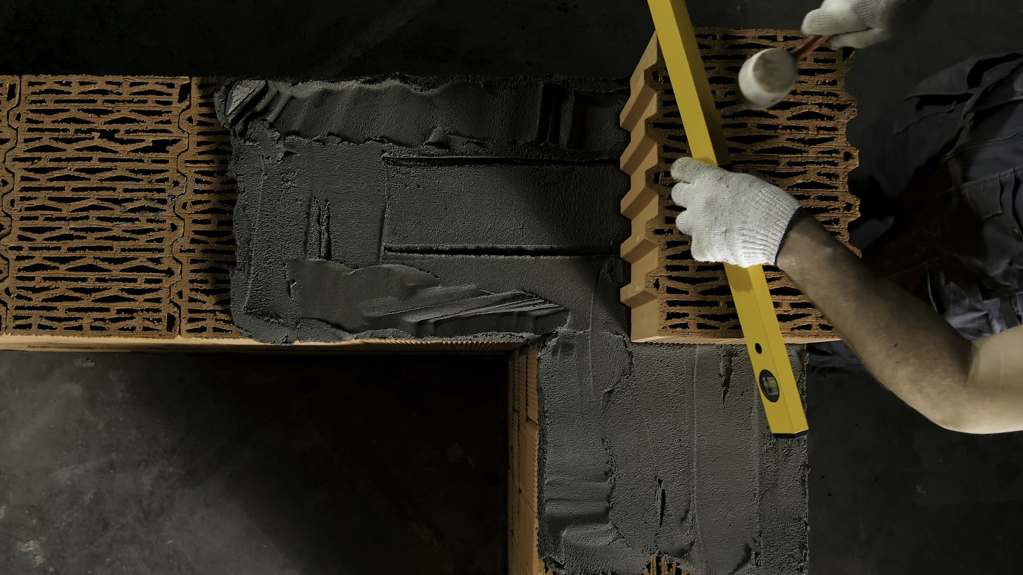 Top view of an industrial worker levelling ceramic brick wall with a wooden hammer. Stock footage